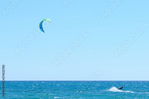 Kitesurfing in the mediterranean sea. Young man performs with an azure and green kitesurf on a clean sky background in a windy sunny day during holydays.