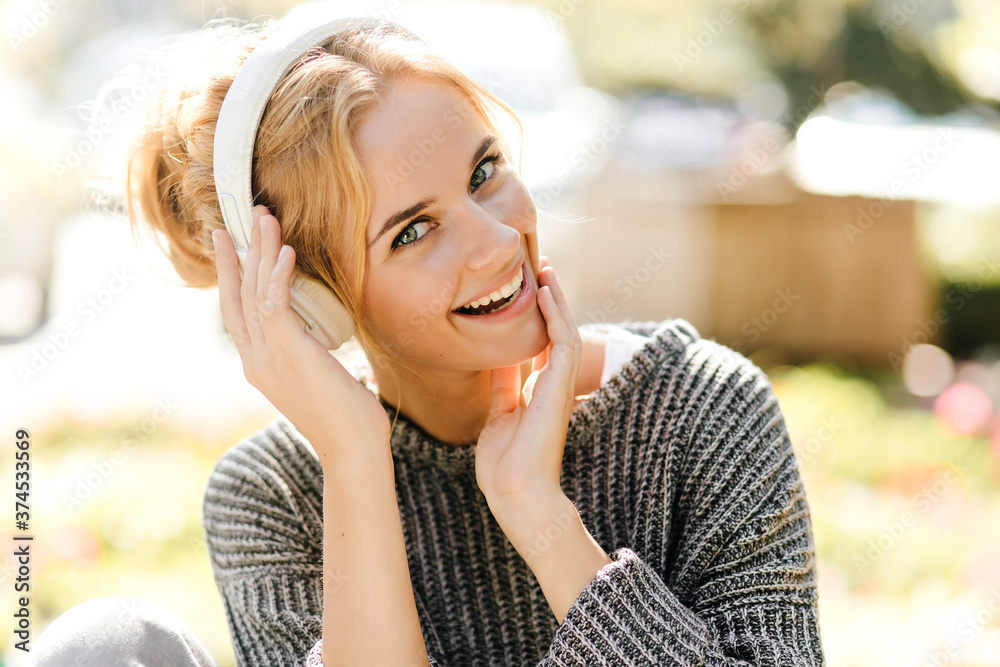 Pretty girl in great mood is laughing while listening to song in big headphones. Snapshot of woman in sweater on street Pretty girl in great mood is laughing while listening to song in big headphones. Snapshot of woman in sweater on street