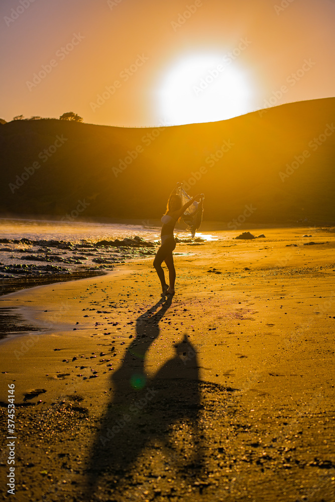 young woman doing yoga during sunrise on the beach