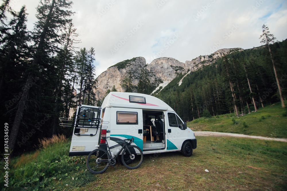 Cute vintage camper van or camping RV parked in wild camping spot in mountain forest. Bicycle off bike rack parked next to converted van. Life on the road in van, outdoor nomadic lifestyle