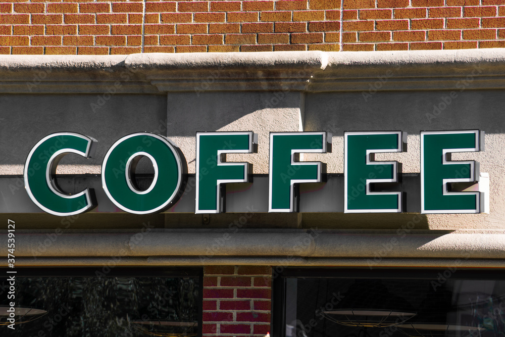 Obraz premium A deep green coffee sign in front of a coffee house with brick walls.