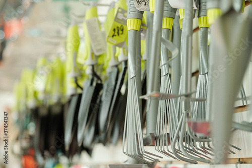 Metallic rakes, shovels and other gardening worktools hanging in row in shop