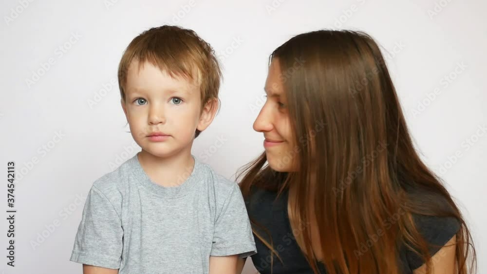 A young beautiful mom kissing her pretty son on the cheek against white background A young beautiful mom kissing her pretty son on the cheek against white background