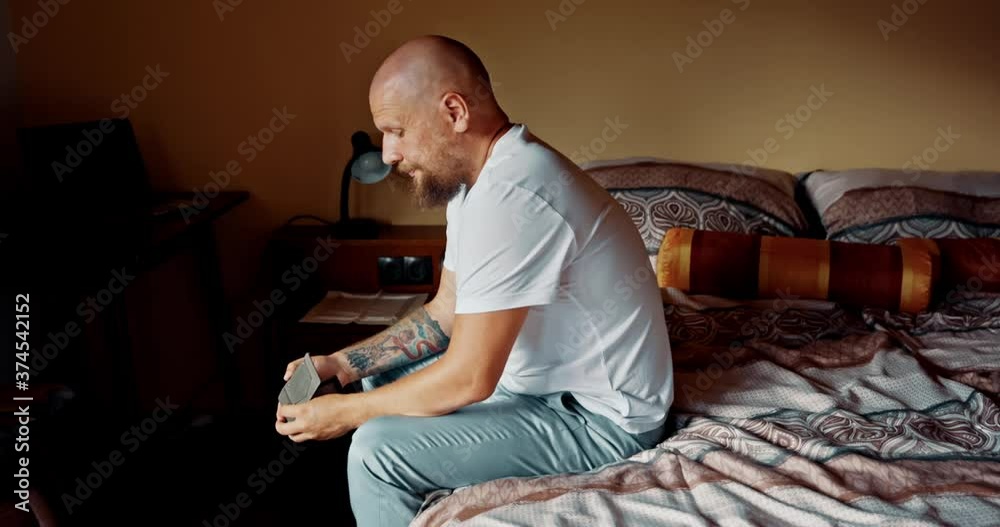 Man sitting on bed looking at empty wallet. Male very dissapointed and depressed feelling hopeless about situation after losing job not able to go on trip. Concept of bankruptcy, poverty, unemployment Man sitting on bed looking at empty wallet. Male very dissapointed and depressed feelling hopeless about situation after losing job not able to go on trip. Concept of bankruptcy, poverty, unemployment