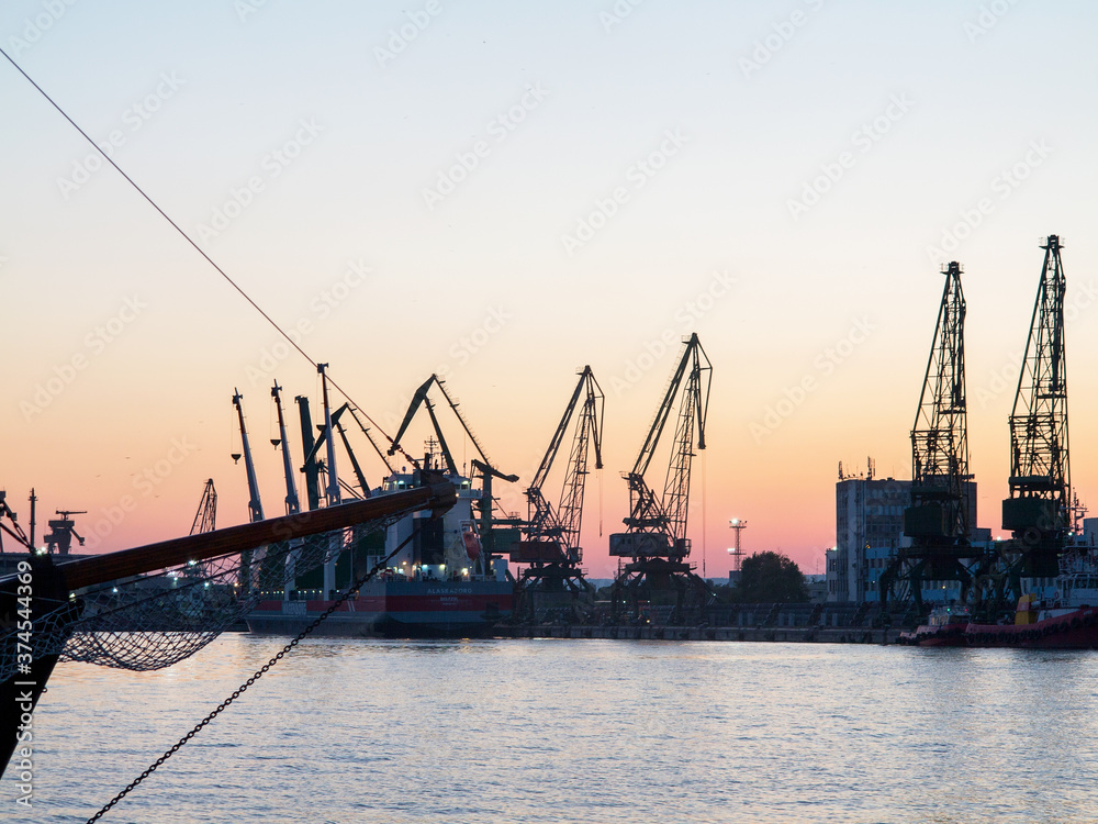 Obraz premium Varna, Bulgaria - July 23, 2016: View on seaport with cranes, cargo and passenger ships at sunset, Varna.