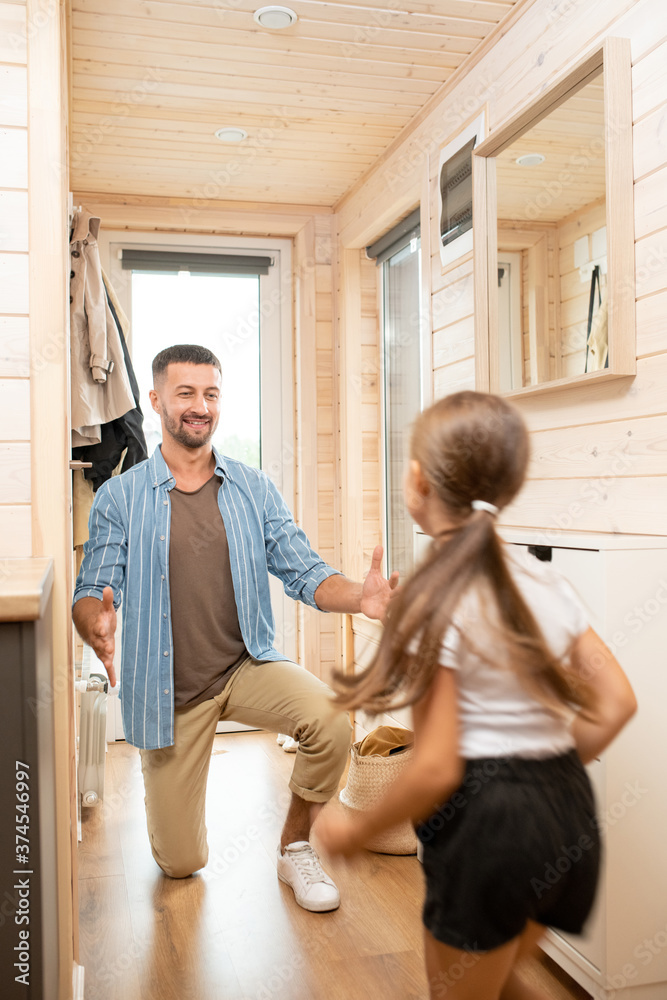 Happy father standing on one knee on the floor while going to embrace daughter