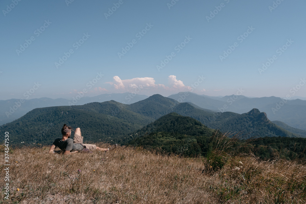 Beautiful mountain and hilly landscape in warm, Sunny weather and the young tourist. A male traveler sits on top of a hill and looks at the surrounding mountains.