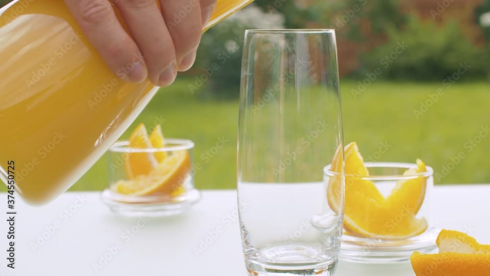 Close up orange juice pouring into the glass and orange pieces in glass jars on the table in the garden. Healthy food, organic vitamins. Close up orange juice pouring into the glass and orange pieces in glass jars on the table in the garden. Healthy food, organic vitamins.