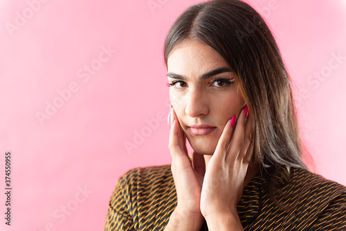 Studio portrait with pink background of a young man with make-up and colorful long nails. photo