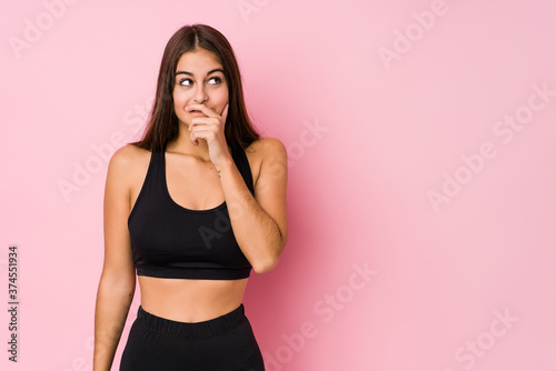 Young caucasian fitness woman doing sport isolated thoughtful looking to a copy space covering mouth with hand.