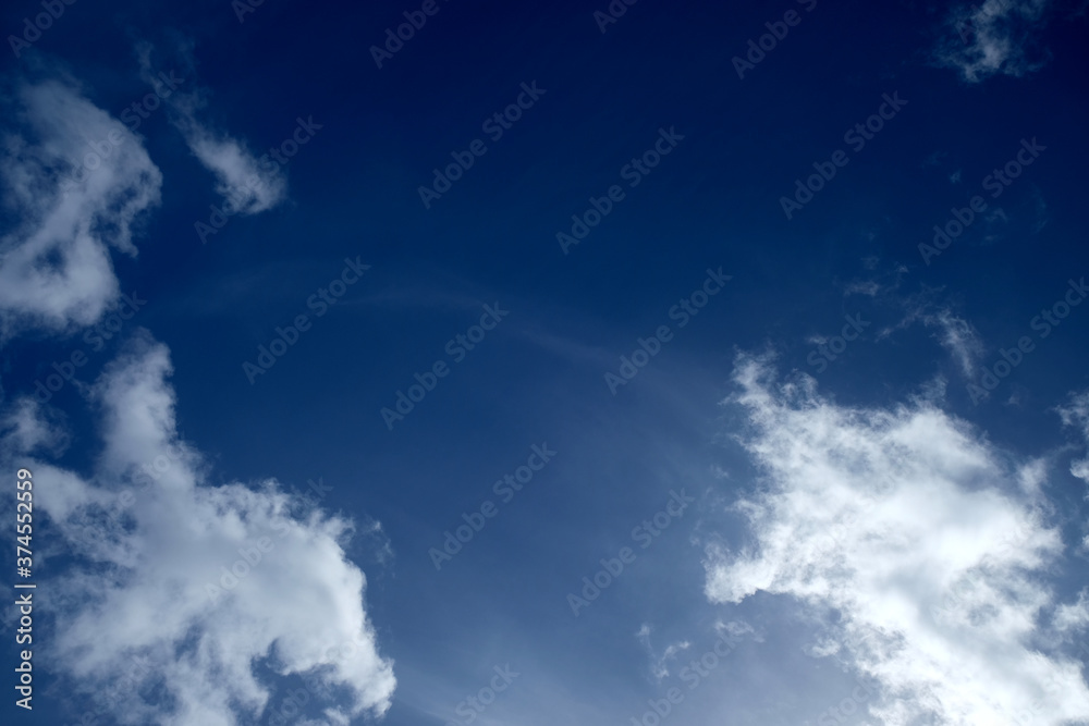 White clouds on intensive blue sky, high cirrus clouds in background, natural sun glare in bottom right corner, polarized light. White clouds on intensive blue sky, high cirrus clouds in background, natural sun glare in bottom right corner, polarized light.