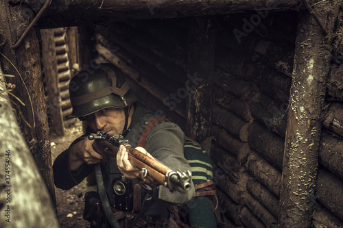 A world war II soldier shoots a rifle from a wooden shelter in the woods. Military historical reconstruction.