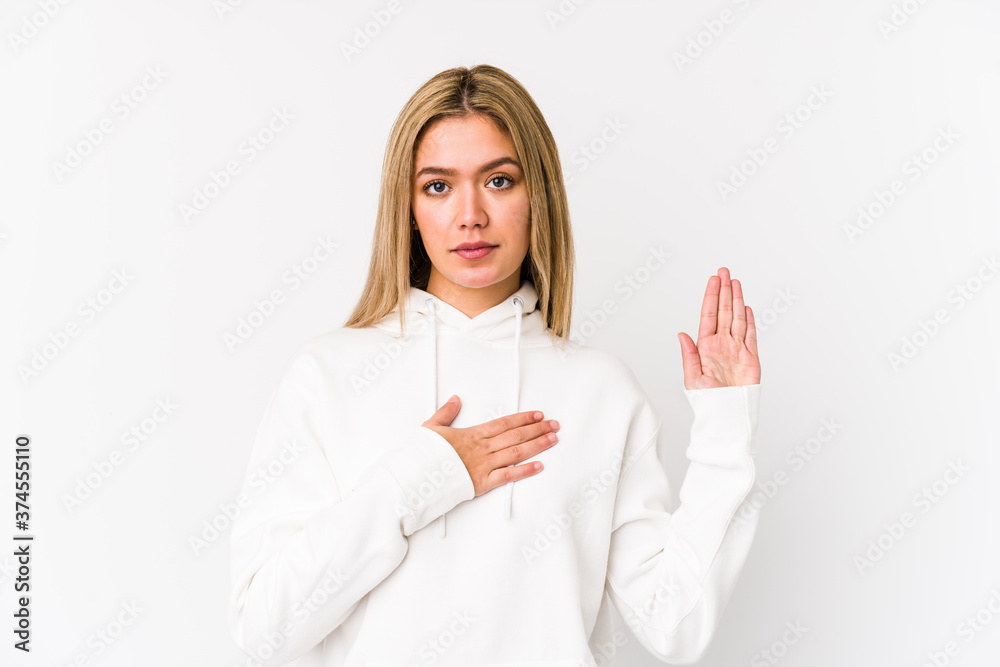 Young blonde caucasian woman isolated taking an oath, putting hand on chest. Young blonde caucasian woman isolated taking an oath, putting hand on chest.