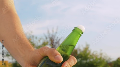 Close up male hand opening bottle of beer using opener outdoors on sky background. The camera slowly moving on the slider