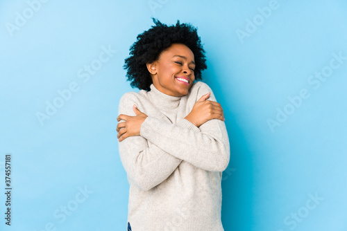 Middle aged african american woman against a blue background isolated hugs, smiling carefree and happy.