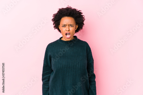 Middle aged african american woman against a pink background isolated screaming very angry and aggressive. © Asier