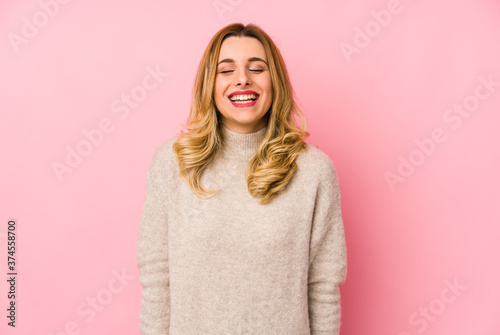 Young blonde cute woman wearing a sweater isolated laughs and closes eyes, feels relaxed and happy.