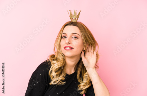 Foto Young blonde woman wearing a crown isolated trying to listening a gossip