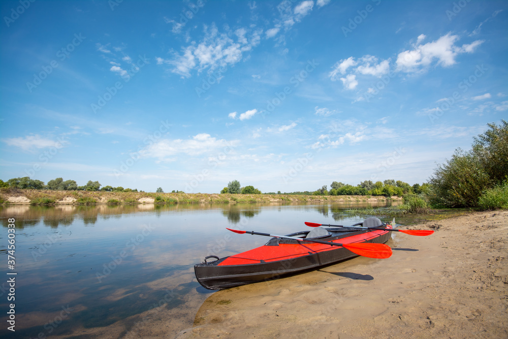 Big red canoe standing on the river shore with two paddles Big red canoe standing on the river shore with two paddles