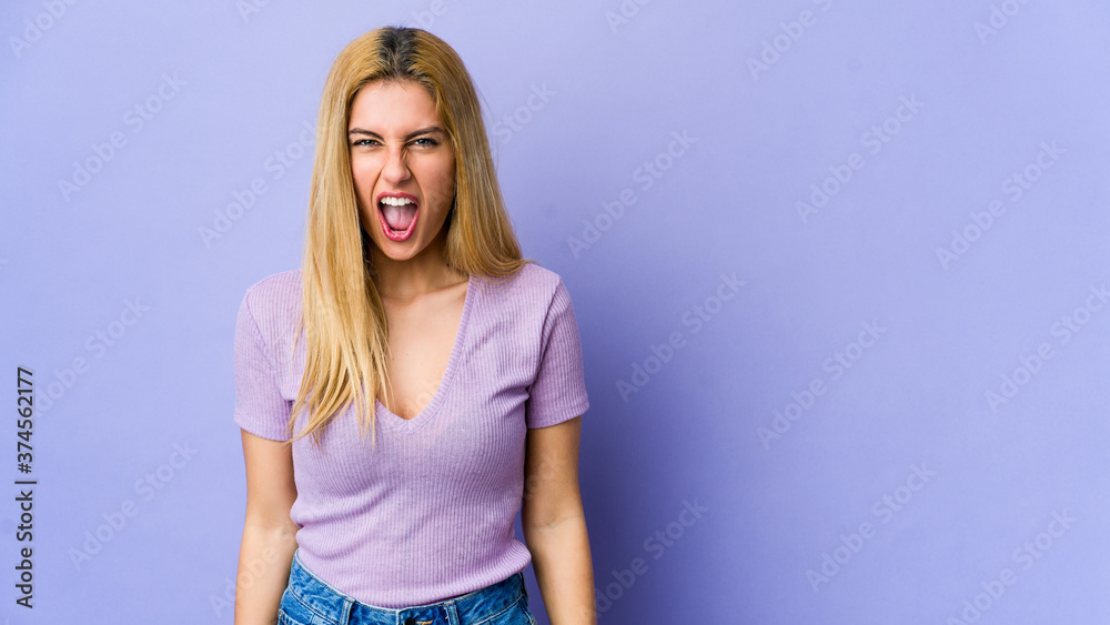 Young blonde woman isolated on purple background shouting very angry, rage concept, frustrated.