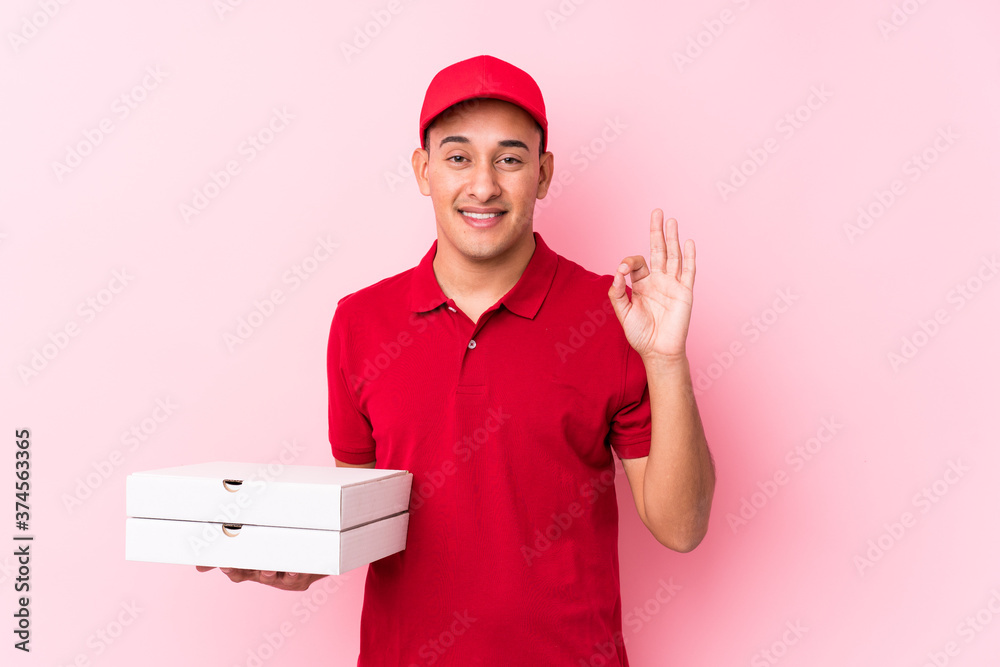 Young pizza delivery latin man isolated cheerful and confident showing ok gesture. Young pizza delivery latin man isolated cheerful and confident showing ok gesture.