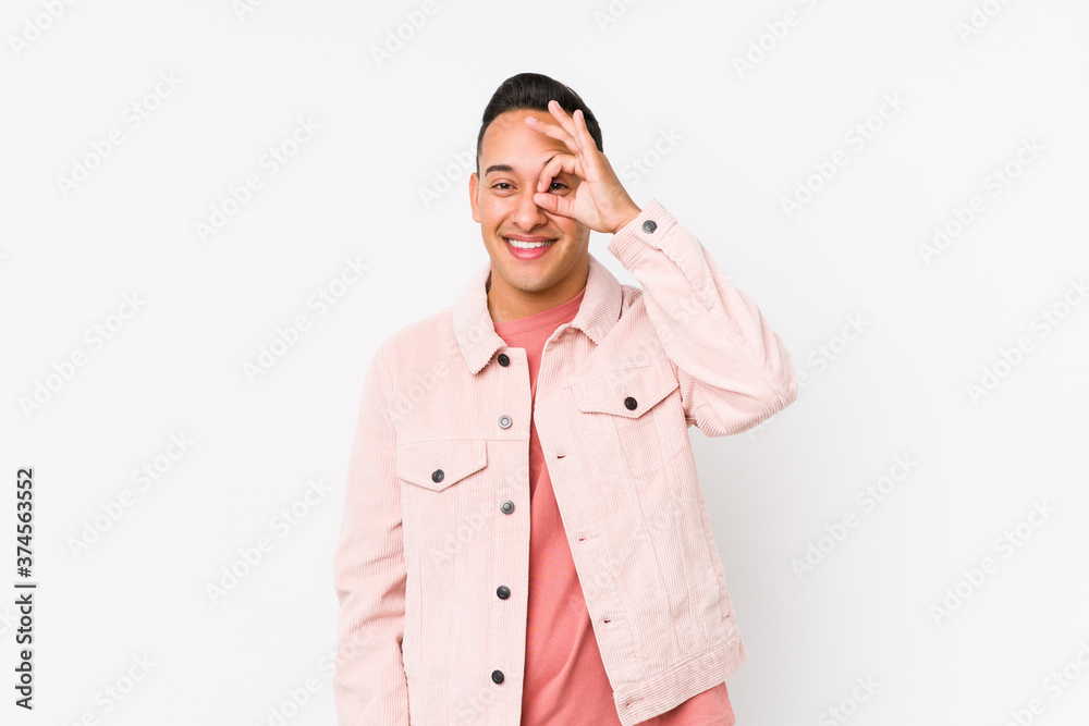 Young latin man posing isolated excited keeping ok gesture on eye. Young latin man posing isolated excited keeping ok gesture on eye.