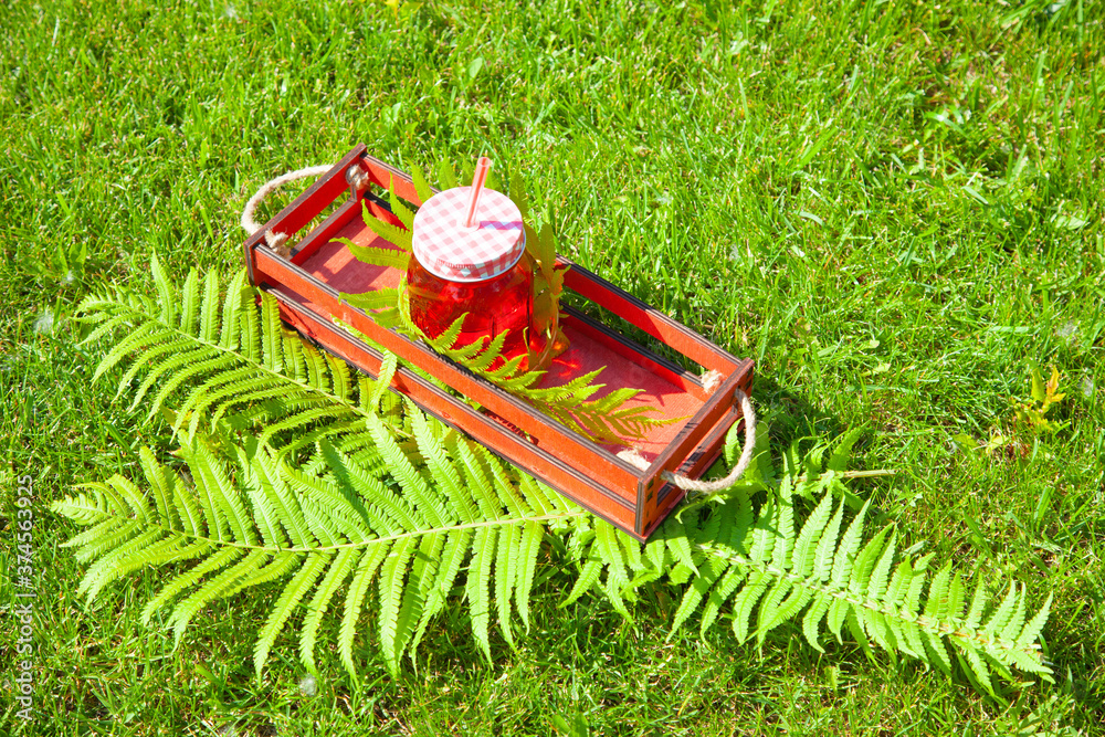 red glass cocktail jar with water or other beverage in a wooden box, fern leaves