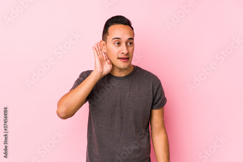 Yooung latin man posing in a pink backgroundtrying to listening a gossip. photo