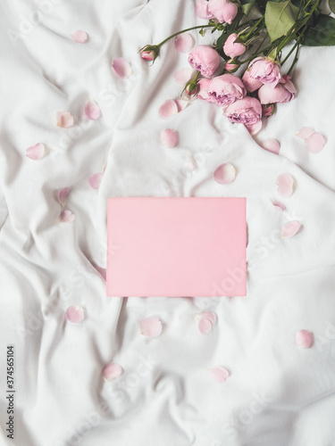 Roses and petals on crumpled white fabric. Natural elegant decoration. Romantic background with copy space on pink envelope. Top view, flat lay.