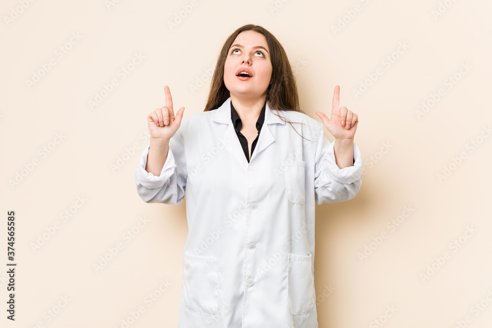 Young doctor woman pointing upside with opened mouth. Young doctor woman pointing upside with opened mouth.