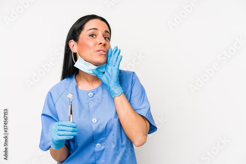 Dentist woman isolated on white background is saying a secret hot braking news and looking aside