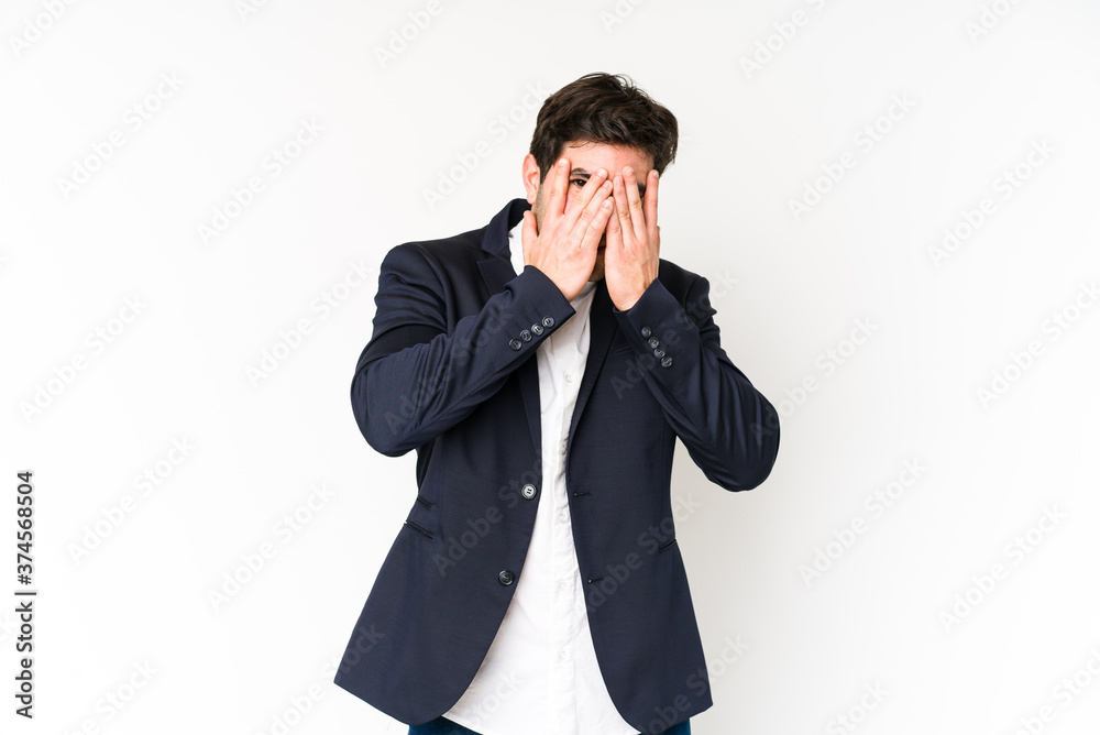 Young business man isolated on white background blink at the camera through fingers, embarrassed covering face.