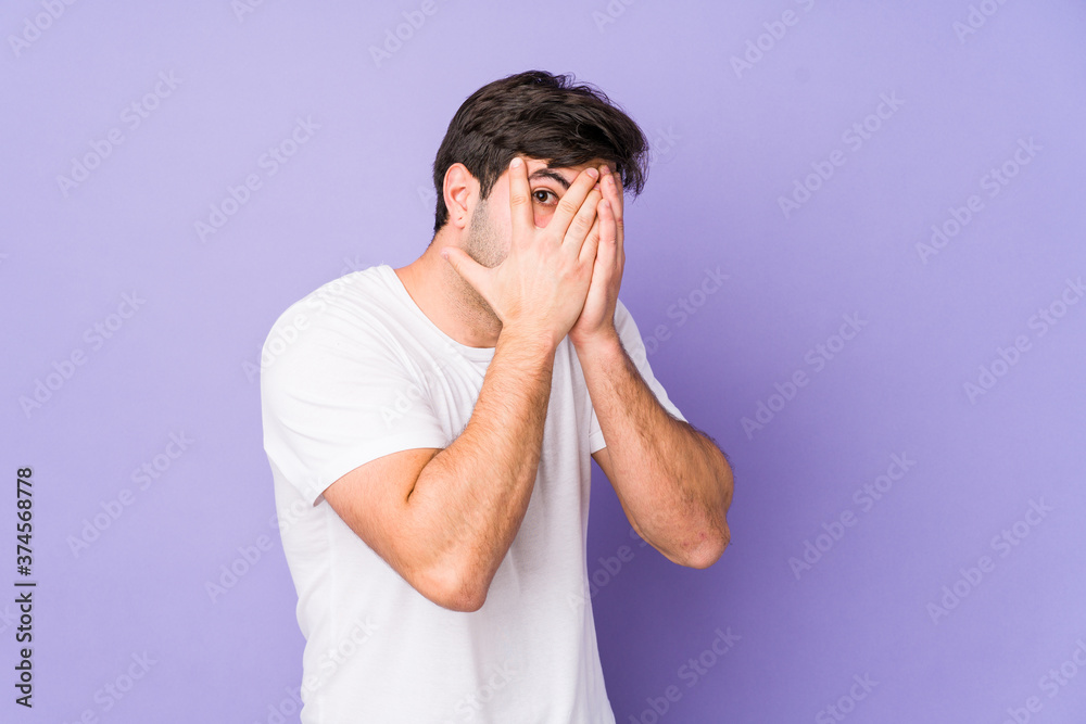 Young man isolated on purple background blink through fingers frightened and nervous. Young man isolated on purple background blink through fingers frightened and nervous.