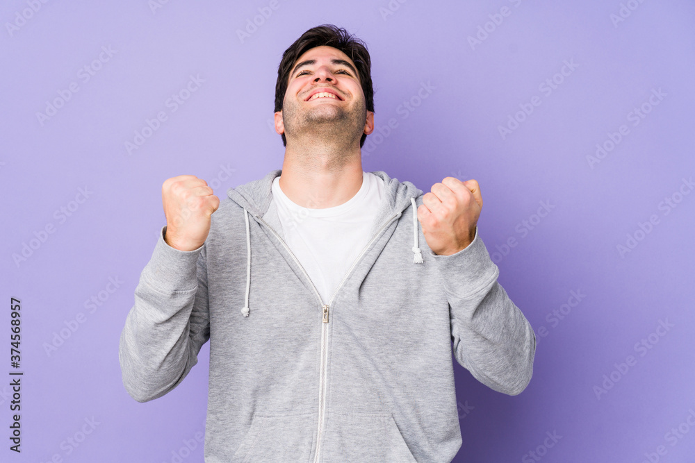 Naklejka premium Young man isolated on purple background celebrating a victory, passion and enthusiasm, happy expression.