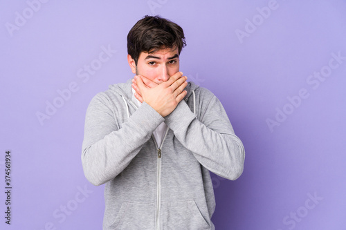 Young man isolated on purple background covering mouth with hands looking worried. © Asier