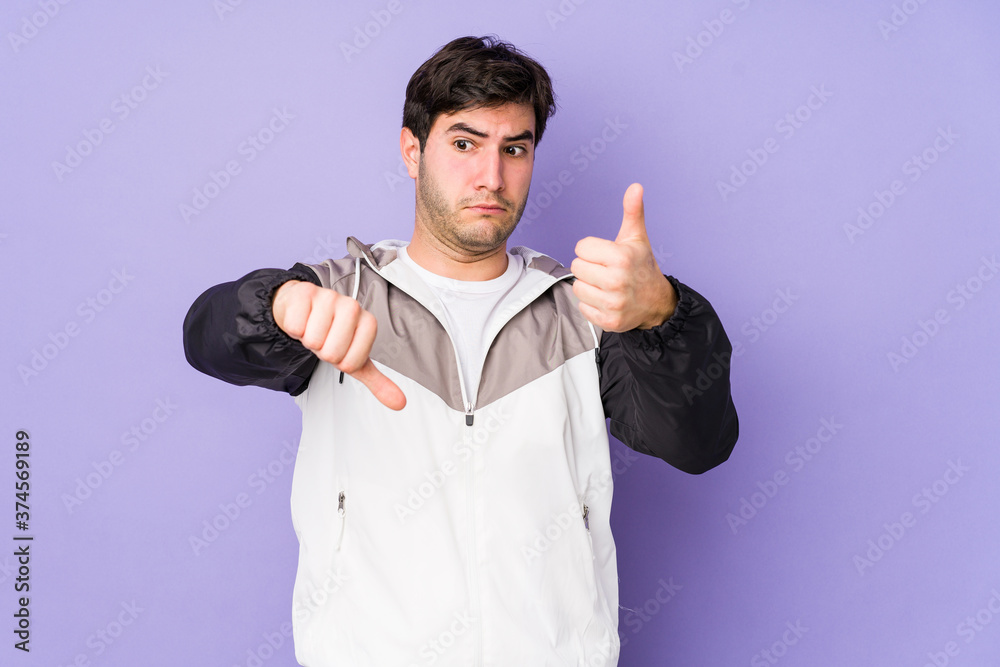 Fototapeta premium Young man isolated on purple background showing thumbs up and thumbs down, difficult choose concept