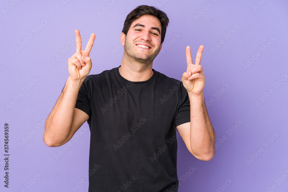 Young man isolated on purple background showing victory sign and smiling broadly. Young man isolated on purple background showing victory sign and smiling broadly.