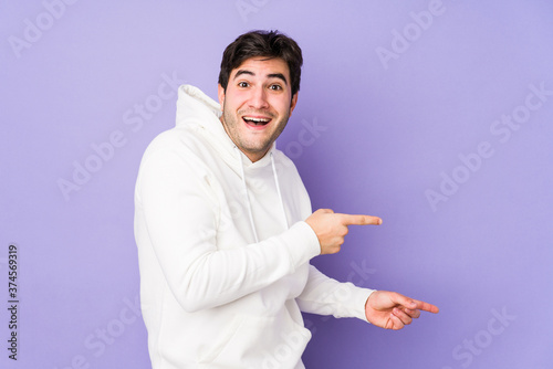 Young man isolated on purple background excited pointing with forefingers away.