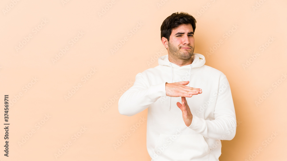 Young man isolated on beige background showing a timeout gesture. Young man isolated on beige background showing a timeout gesture.
