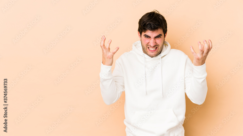 Fototapeta premium Young man isolated on beige background screaming with rage.