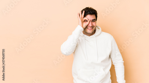 Young man isolated on beige background excited keeping ok gesture on eye.