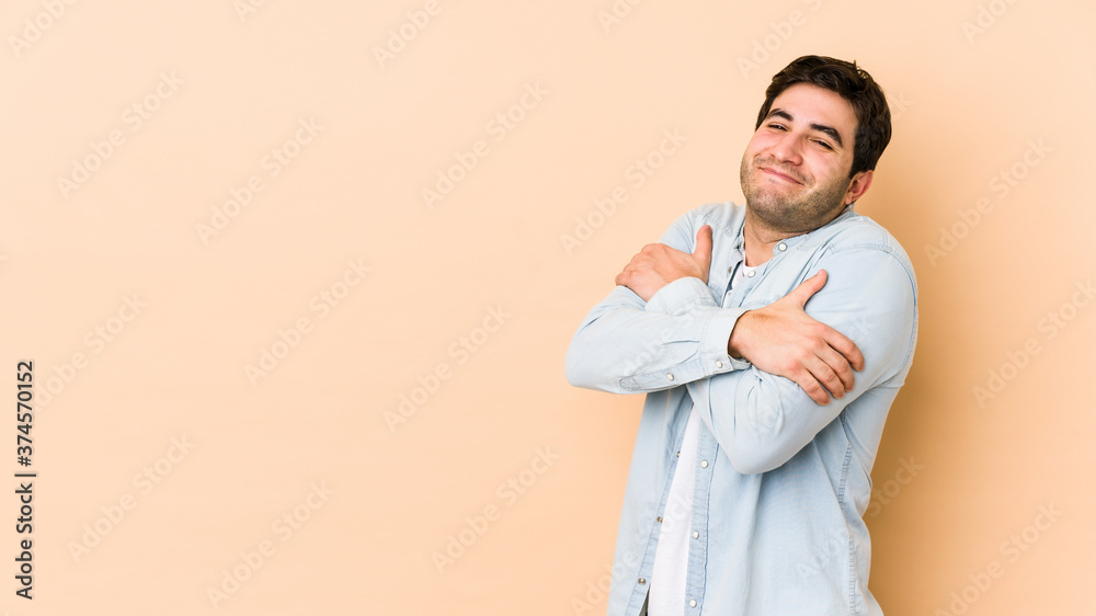 Young man isolated on beige background hugs, smiling carefree and happy. Young man isolated on beige background hugs, smiling carefree and happy.