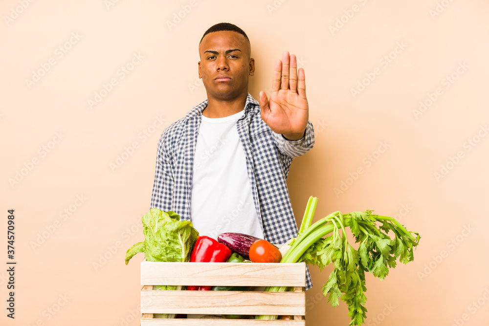 Young farmer man isolated on a beige background standing with outstretched hand showing stop sign, preventing you. Young farmer man isolated on a beige background standing with outstretched hand showing stop sign, preventing you.