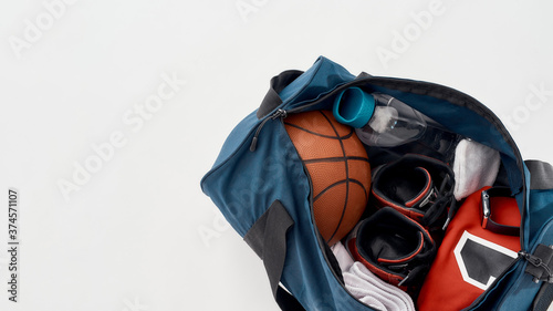 Basketball training set. Top view of a sports bag with professional uniform, basketball ball, sneakers and bottle of water isolated on grey background