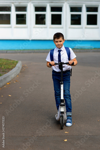 portrait of a handsome stylish and young schoolboy in a white shirt, blue tie and a backpack with a scooter © Natasha 