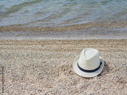 A white straw hat lies on the sand by the water. Sea beach on a summer sunny day. Sea vacation concept. Copy space. High quality photo