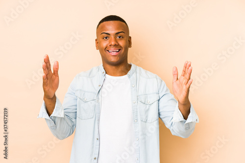 Young latin man isolated on beige background receiving a pleasant surprise, excited and raising hands. © Asier