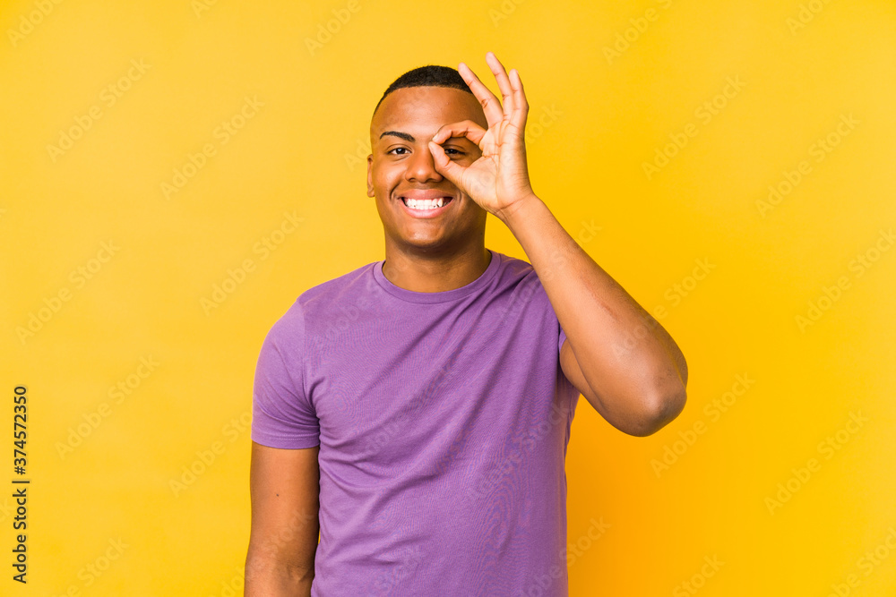 Fototapeta premium Young latin man isolated on yellow background excited keeping ok gesture on eye.