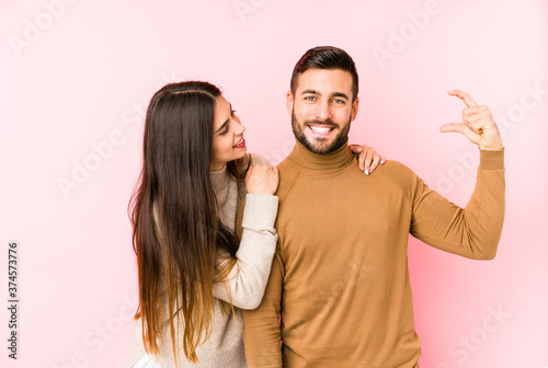 Young caucasian couple isolated holding something little with forefingers, smiling and confident.