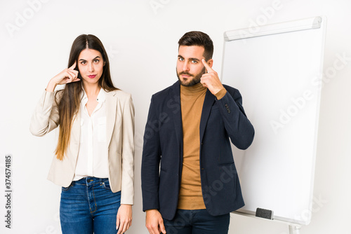Young caucasian business couple isolated pointing temple with finger, thinking, focused on a task.